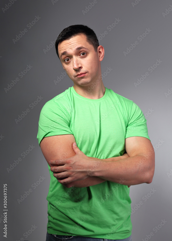 Thinking casual doubt young man with folded arms in green shirt on grey backgrond. Thinking casual doubt young man with folded arms in green shirt on grey backgrond.