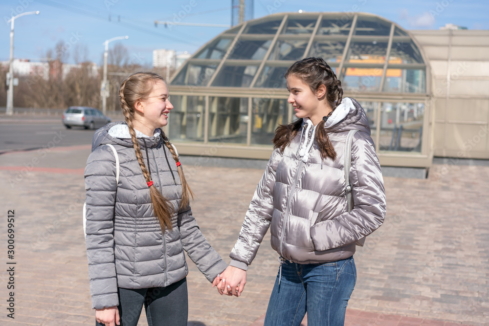 two best girlfriends in warm gray jacket holds hand standing at city street subway entrance background