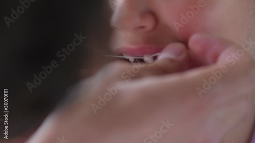 The hands of an adult tie a thread to a child's tooth. Pull out the tooth with a thread. Remove the tooth at home. The girl is afraid and does not want to pull out the tooth. Close up