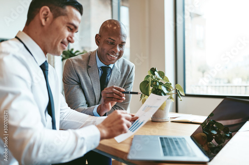 Fotografie Two diverse businessmen going over graphs together in an office