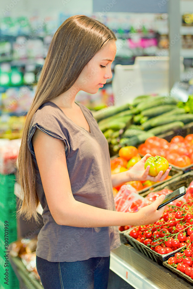 Teen girl shopping in supermarket, reading product information. Choosing daily product. Concept of healthy food, bio, vegetarian, diet.
