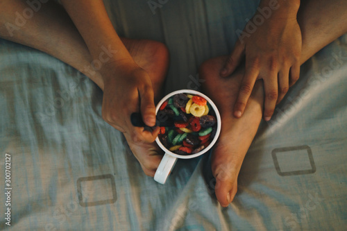 Young child having breakfast and eating colorful cereals in bed.