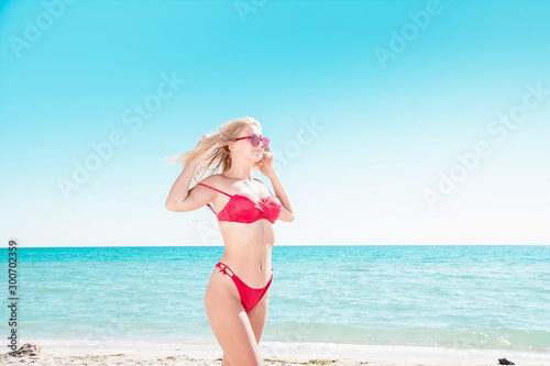 Portrait of a blonde in pink glasses at the sea. A woman walks along the beach and enjoys. © Haibullaev