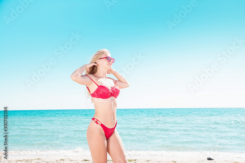 Portrait of a blonde in pink glasses at the sea. A woman walks along the beach and enjoys.