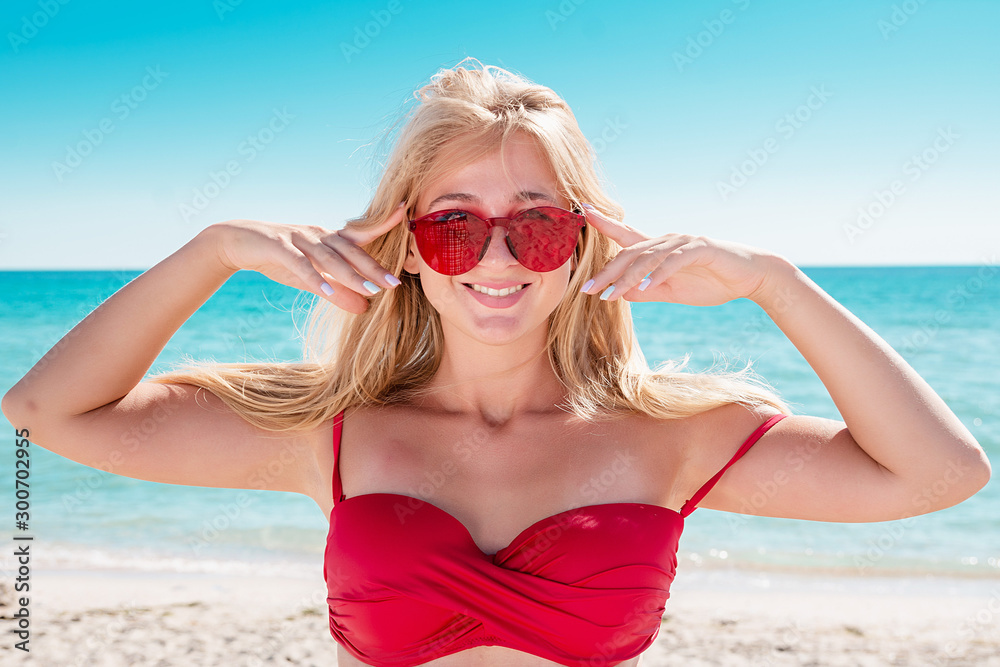Portrait of a blonde in pink glasses at the sea. A woman walks along the beach and enjoys. Portrait of a blonde in pink glasses at the sea. A woman walks along the beach and enjoys.