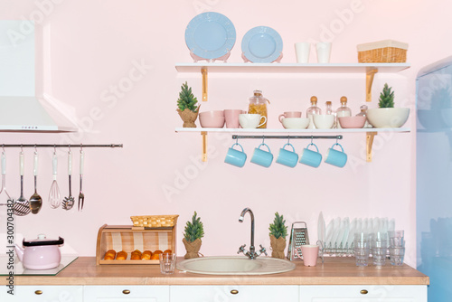 Pink and blue pastel modern kitchen interior. Kitchen accessories, containers with cereals, dishes and hanging blue cups.