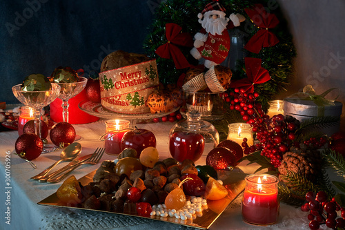 Christmas or New Year in the light of candles with sweets, red and gold ornaments specific for these dates on a white thread tablecloth background.