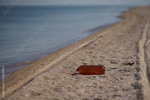 Empty plastic bottle lying on the sea beach. Environmental pollution. Tire tracks on the sand. photo