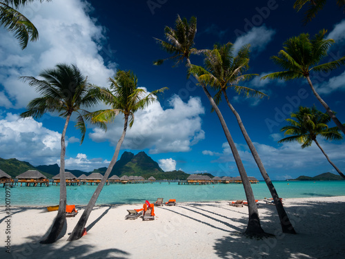 Luxury overwater villas with palm trees, blue lagoon, white sandy beach and Otemanu mountain at Bora Bora island, Tahiti, French Polynesia.