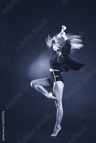 Beautiful gymnast athlete teenage girl wearing dancer colorful leotard working out, dancing, posing, sitting in splits, doing backbend art gymnastics exercise, studio, dark background