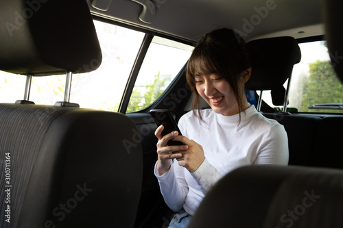 Asian teenager woman using a smartphone in back seat of car, Passengers use an app to order a ride and Peer-to-peer ride sharing concept © comzeal