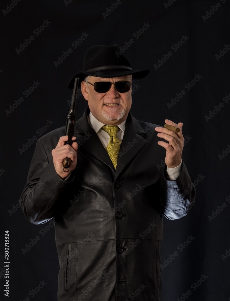 A man in black clothes, a black leather coat, hat. Ganster with a cigar Mauser system pistol. Mafiosi in black glasses on a dark background. Severe, strong, stylish, impressive, dangerous, unfriendly A man in black clothes, a black leather coat, hat. Ganster with a cigar Mauser system pistol. Mafiosi in black glasses on a dark background. Severe, strong, stylish, impressive, dangerous, unfriendly