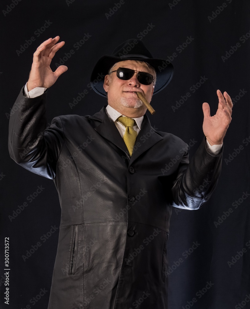 A man in black clothes, a black leather coat, hat. Ganster with a cigar. Mafiosi in black glasses on a dark background. Severe, strong, stylish, impressive, dangerous, unfriendly, evil, rude man A man in black clothes, a black leather coat, hat. Ganster with a cigar. Mafiosi in black glasses on a dark background. Severe, strong, stylish, impressive, dangerous, unfriendly, evil, rude man