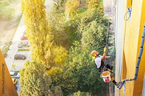Industrial rope access worker hanging from the building while painting the exterior facade wall. Industrial alpinism concept image. Top view