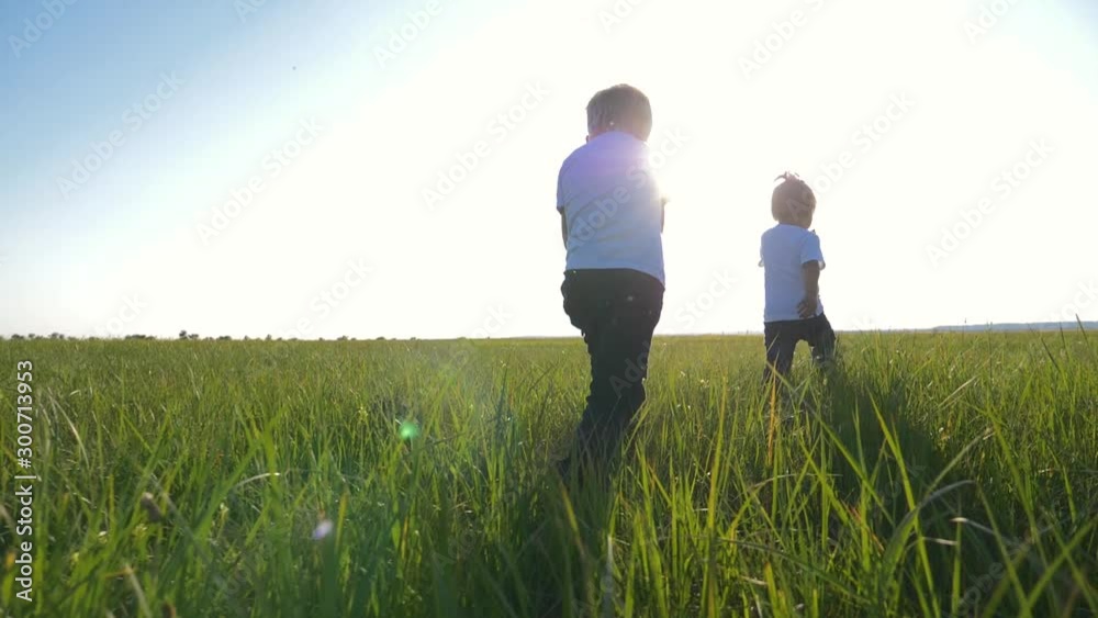 Two children in white t-shirts running on green fresh grass. Happy children enjoy life. The concept of teamwork. Two children in white t-shirts running on green fresh grass. Happy children enjoy life. The concept of teamwork.