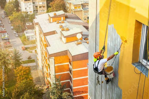 Industrial rope access worker hanging from the building while painting the exterior facade wall. Industrial alpinism concept image. Top view