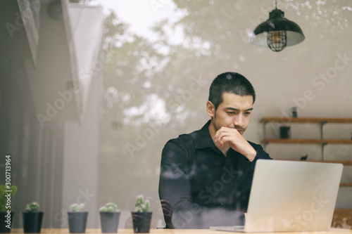Portrait of a young business man using laptop computer while working. Young asian business men working with laptop in coffee shop cafe.