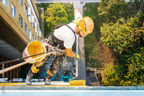 Industrial rope access worker hanging from the building while painting the exterior facade wall. Industrial alpinism concept image. Top view