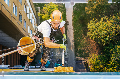 Industrial rope access worker hanging from the building while painting the exterior facade wall. Industrial alpinism concept image. Top view