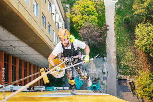Industrial rope access worker hanging from the building while painting the exterior facade wall. Industrial alpinism concept image. Top view