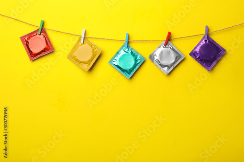 Colorful condoms hanging on clothesline against yellow background, space for text. Safe sex concept photo