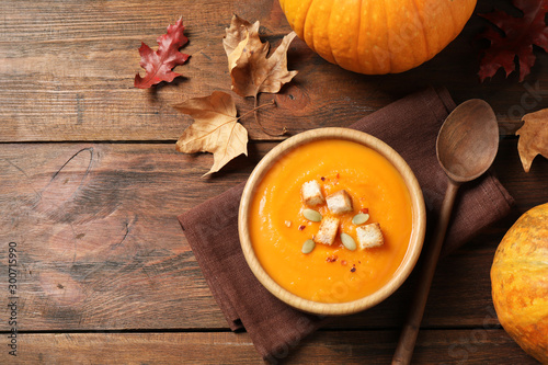 Bowl with tasty pumpkin cream soup on wooden table, flat lay. Space for text