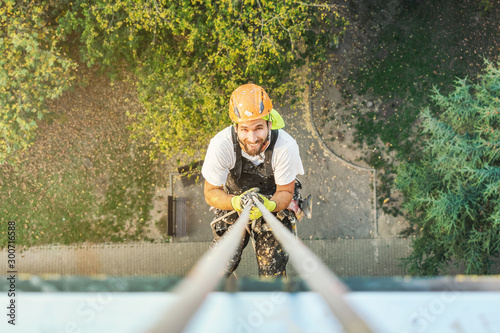Industrial rope access worker hanging from the building while painting the exterior facade wall. Industrial alpinism concept image. Top view