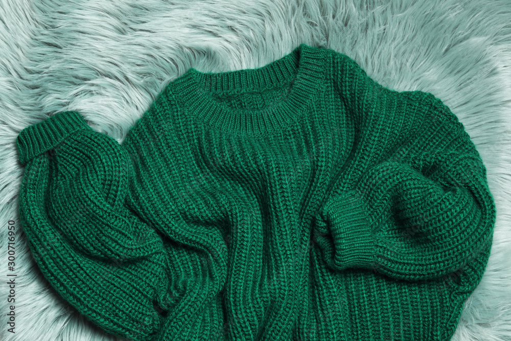 Fototapeta premium Soft knitted sweater on green fur rug, flat lay
