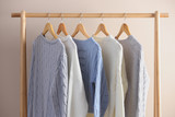 Collection of warm sweaters hanging on rack near light wall