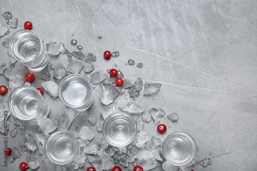 Shots of vodka, cranberries and ice on grey background, flat lay. Space for text - obrazy, fototapety, plakaty 