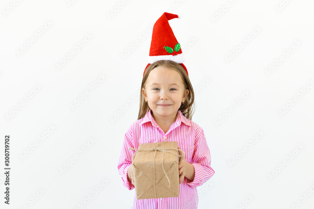 Smiling funny child in Santa red hat holding gift box in hand over white background with copyspace. Christmas concept. Smiling funny child in Santa red hat holding gift box in hand over white background with copyspace. Christmas concept.