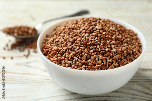 Bowl of uncooked buckwheat on white wooden table