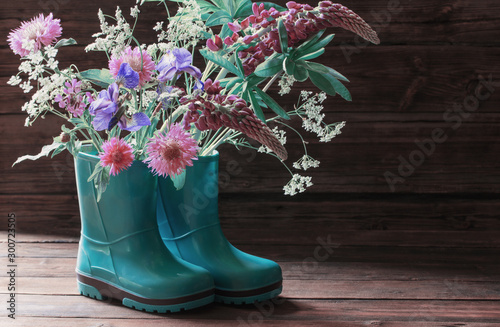summer flowers in rubber boots on old dark wooden background