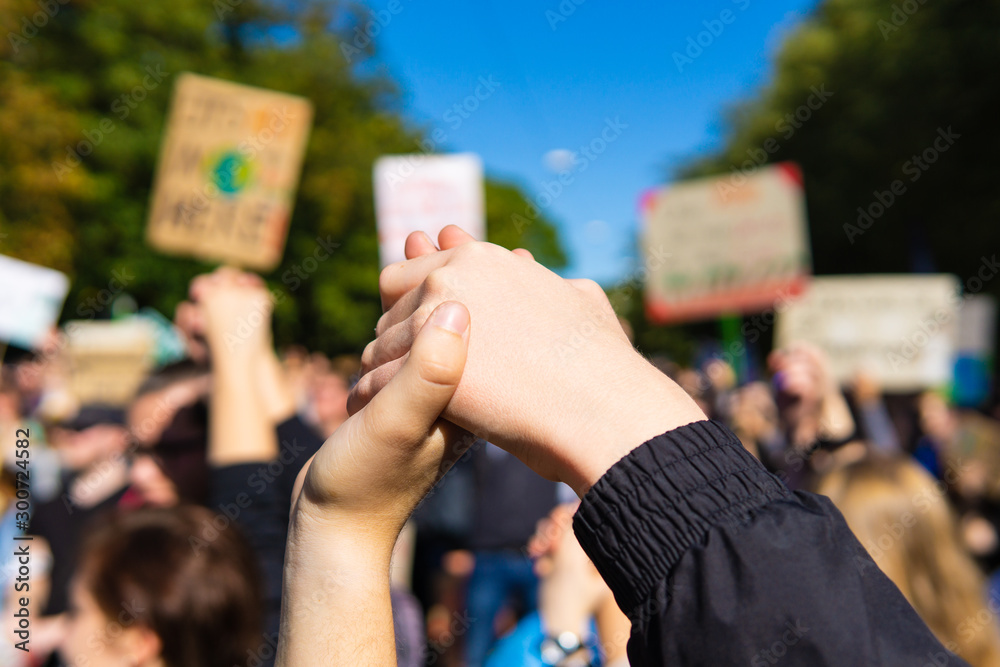 two young people at a rally, joining hands together signaling peace, unity  and decisiveness in front of a crowd carrying protest placards with shallow  depth of field Stock Photo | Adobe Stock