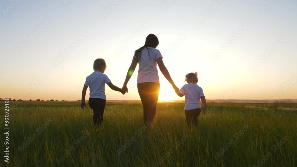 A young woman mother walks with two young children on the grass in the Park. A happy family walks outdoors in the setting sun. A young woman mother walks with two young children on the grass in the Park. A happy family walks outdoors in the setting sun.