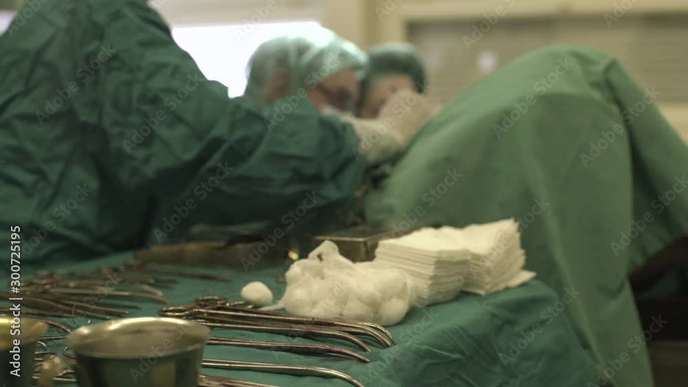 Nurse assisting team of surgeons during operation of patient in operating room, rack focus, close up.