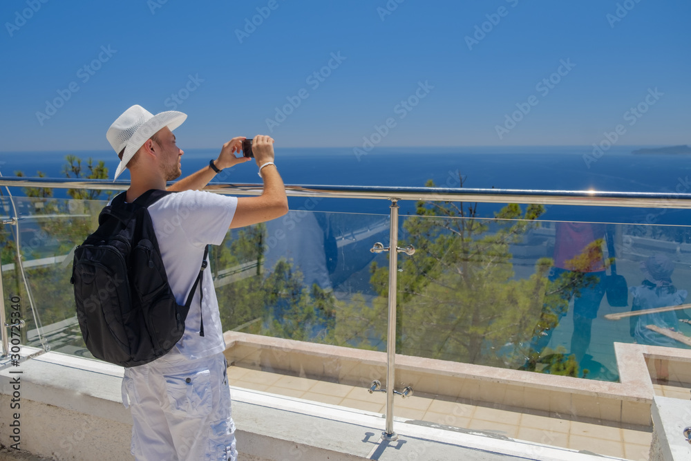 tourist in a white hat and white clothes makes selfie phone on the background of panorama of mountains and the sea