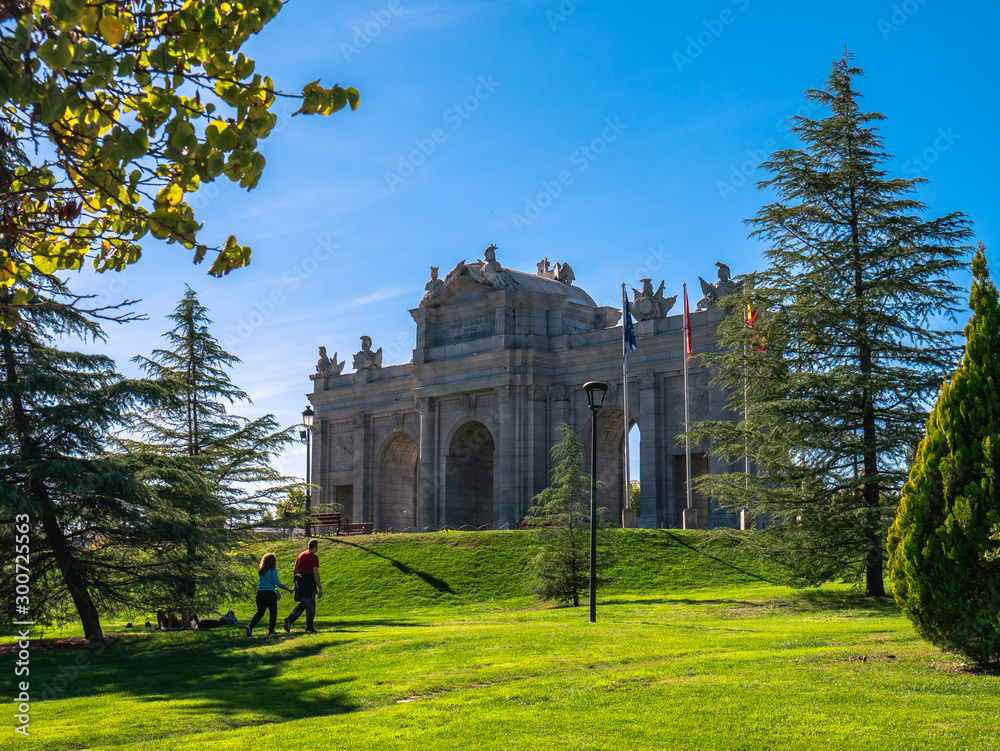 Fototapeta premium Replica of the Puerta de Alcala in Madrid, in the Europa park of Torrejon de Ardoz, surrounded by trees and a beautiful blue sky in the background