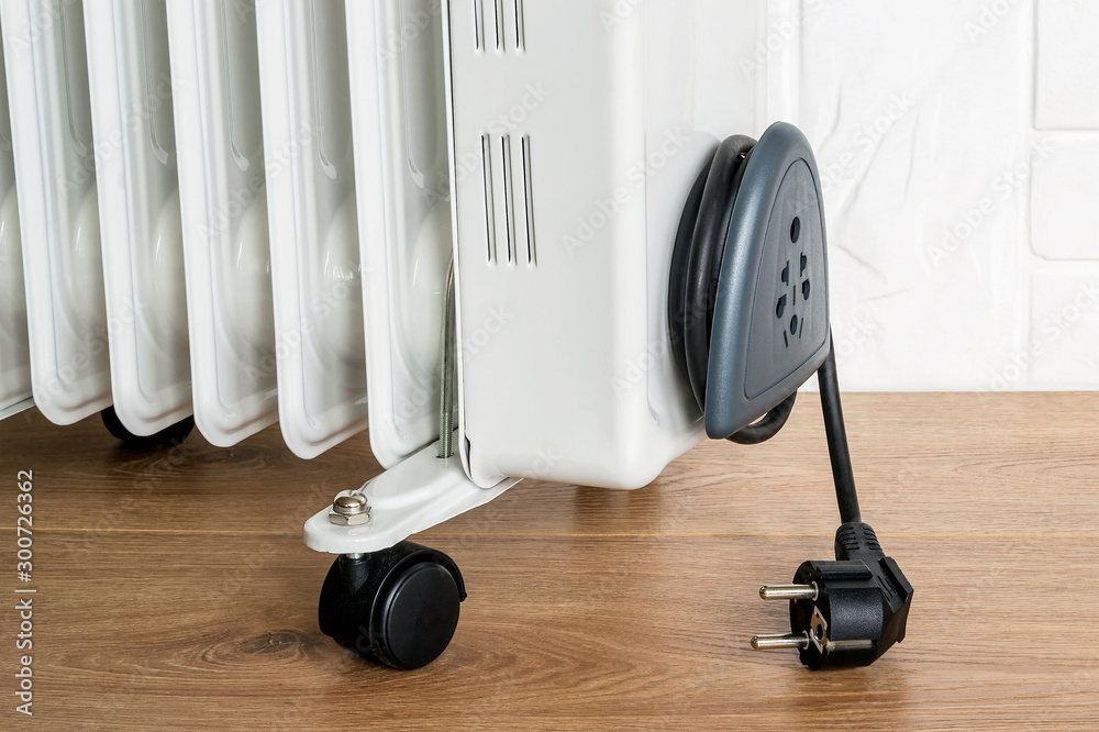 Home electric oil heater on plastic twin wheels and with cable reeled up on  a cable storage. White oil-filled radiator on a brown wooden floor. Stock  Photo | Adobe Stock