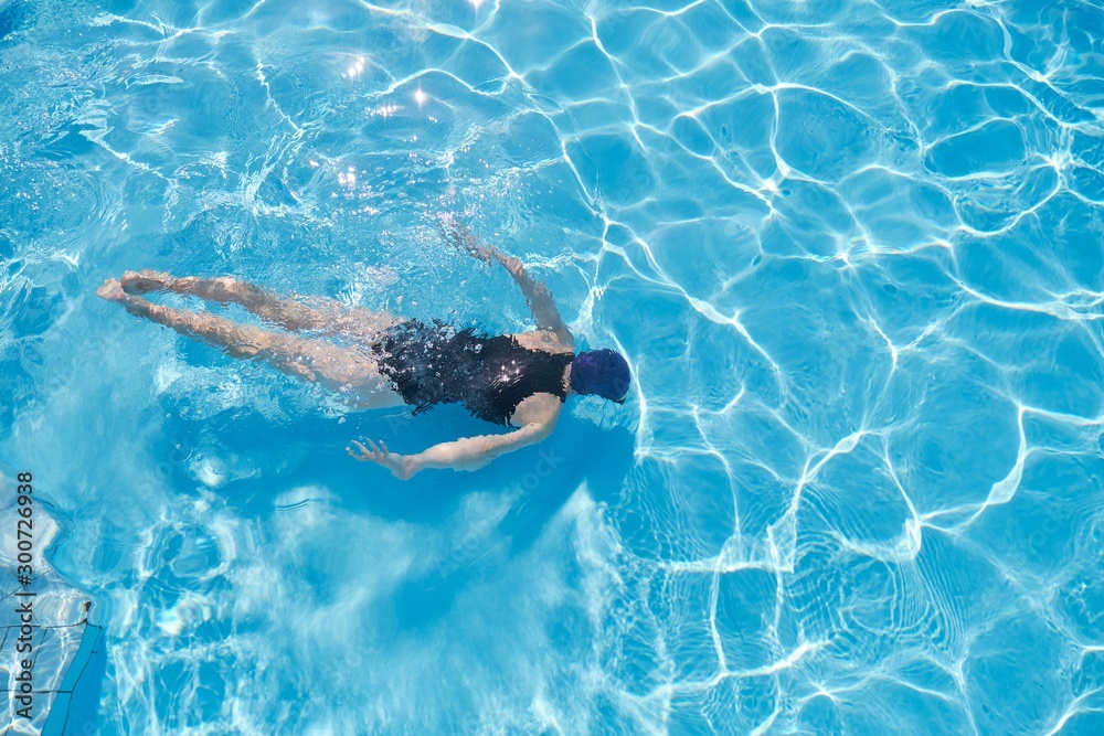 Young woman swimming underwater in an outdoor pool, top view of back of girl