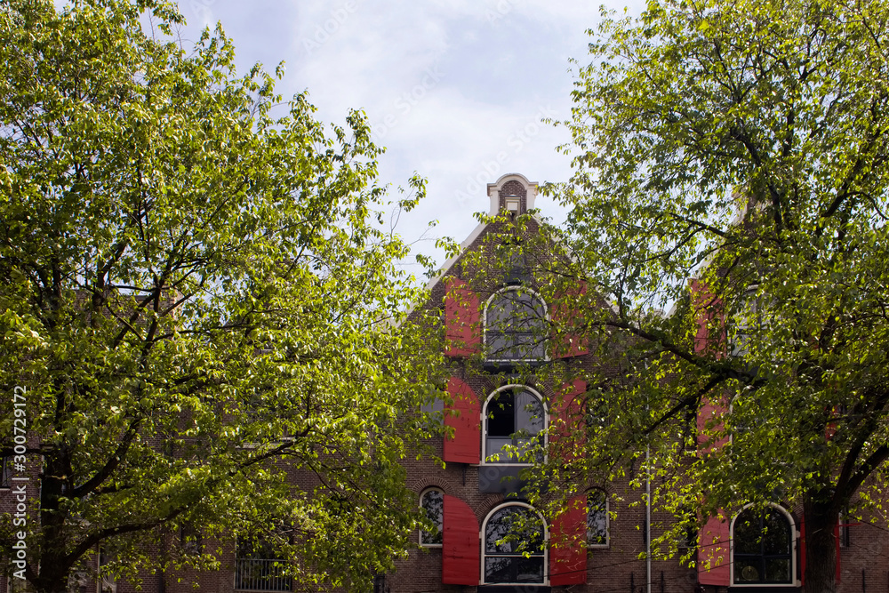 View of historical, traditional and typical buildings showing Dutch architectural style and trees in Amsterdam. It is a sunny summer day. View of historical, traditional and typical buildings showing Dutch architectural style and trees in Amsterdam. It is a sunny summer day.