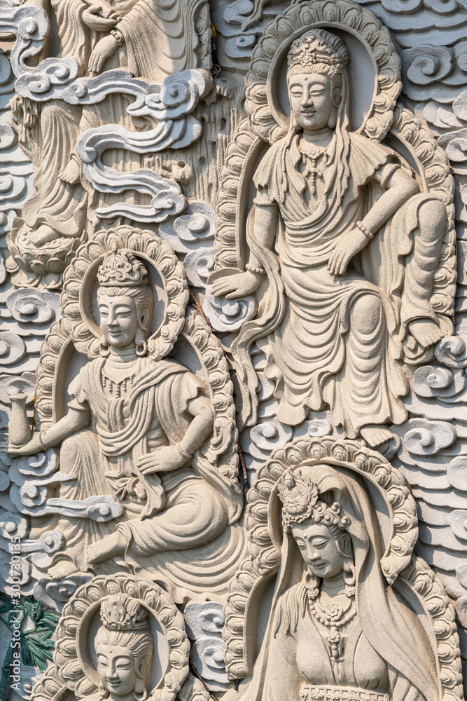 Da Nang, Vietnam - March 10, 2019: Chua An Long Chinese Buddhist Temple. Gray stone happy  multiple different Bodhisattvas fresco as backdrop for Guan Yin statue, not in picture.