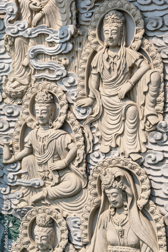 Da Nang, Vietnam - March 10, 2019: Chua An Long Chinese Buddhist Temple. Gray stone happy multiple different Bodhisattvas fresco as backdrop for Guan Yin statue, not in picture.