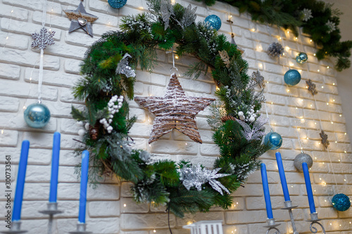 Christmas and New Year living room interior with decorated firtree wreath, toys, blue candles, star and garland lights