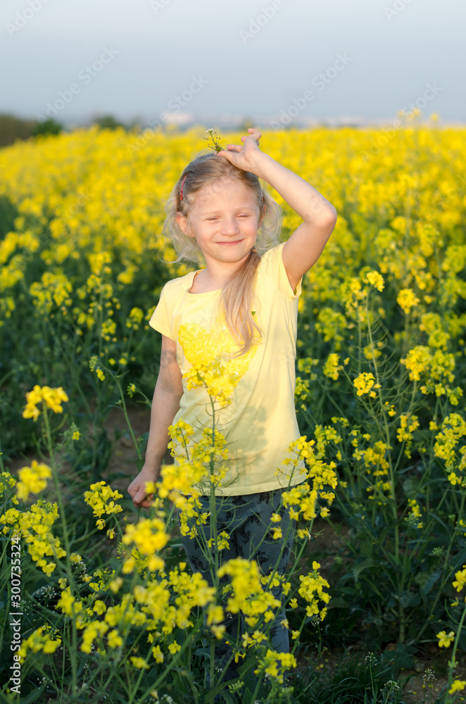 adorable charming blond girl with hands up in yellow meadow