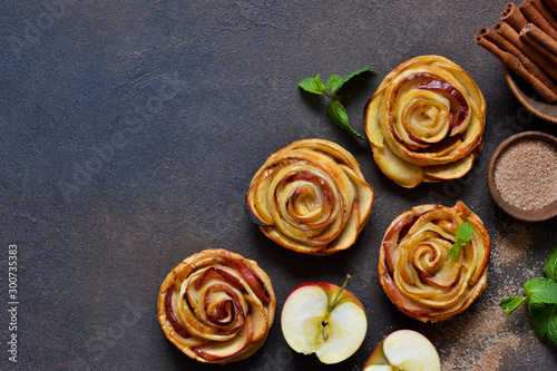 Dish of apple roses baked in puff pastry on a dark concrete background with apples. View from above