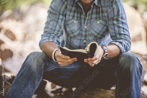 Closeup shot of a male in casual clothing reading the holy bible on a blurred background