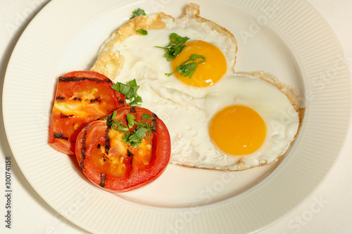 morning food fried eggs from two eggs and slices of grilled tomato on a white plate, white background © shediva