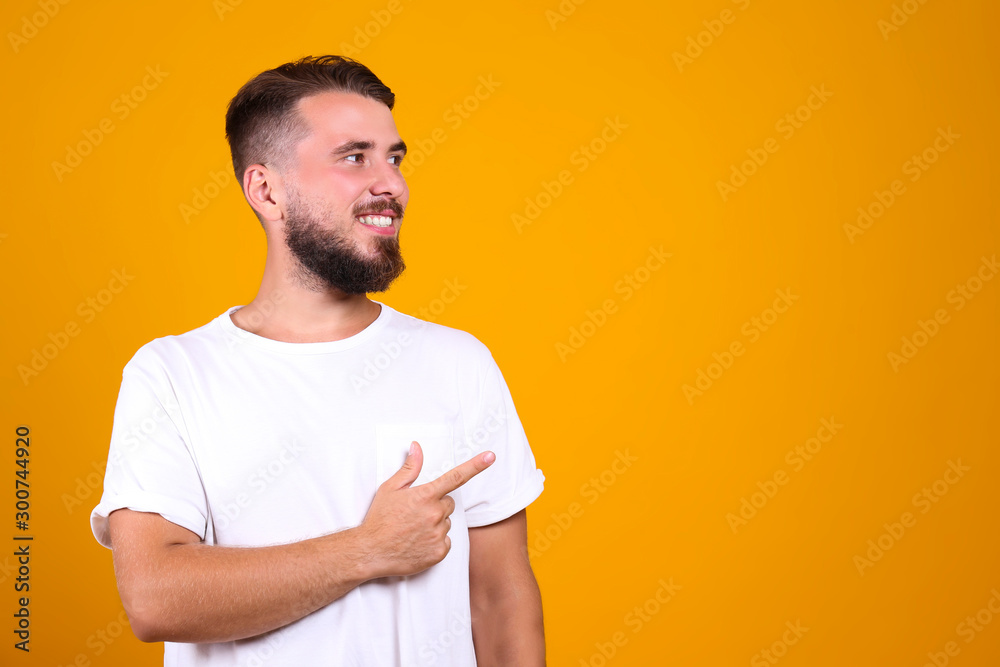Young handsome man with facial hair posing yellow gray wall with a lot of copy space for text. Portrait of confident bearded male, wearing blank white oversized t-shirt. Isolated, background. Young handsome man with facial hair posing yellow gray wall with a lot of copy space for text. Portrait of confident bearded male, wearing blank white oversized t-shirt. Isolated, background.