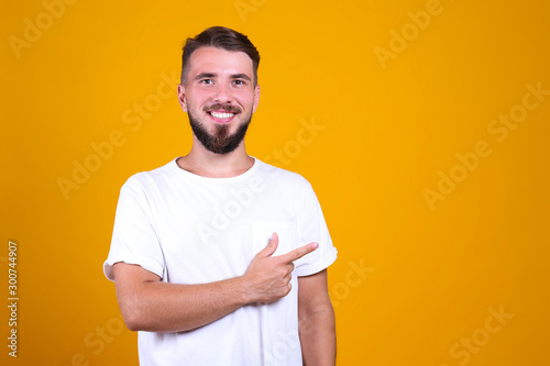 Young handsome man with facial hair posing yellow gray wall with a lot of copy space for text. Portrait of confident bearded male, wearing blank white oversized t-shirt. Isolated, background.
